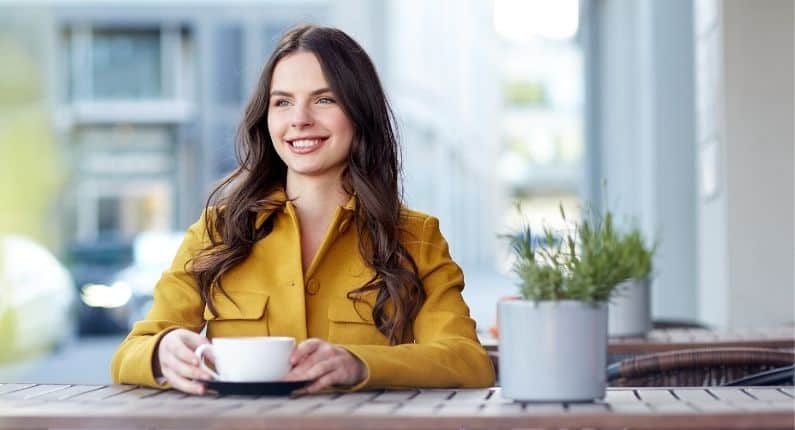 Life changing habits | Woman in yellow jacket smiling with a coffee